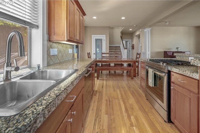 kitchen with gas stove, a sink, light wood-type flooring, brown cabinets, and backsplash