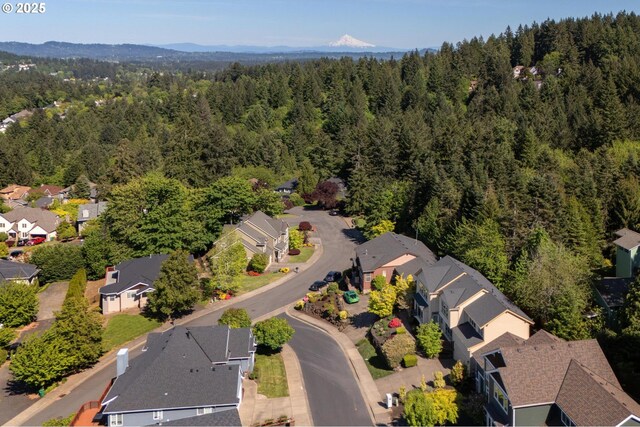 aerial view of property and surrounding area featuring a forest, nearby suburban area, and a mountainous background