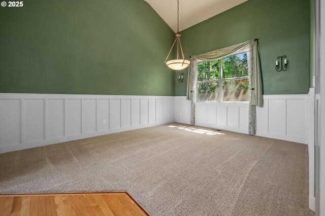 unfurnished dining area featuring wainscoting, carpet floors, a decorative wall, and high vaulted ceiling