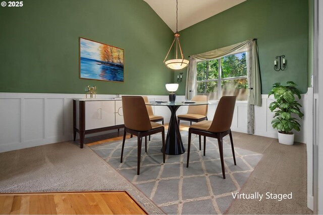 carpeted dining space featuring a decorative wall, lofted ceiling, and a wainscoted wall