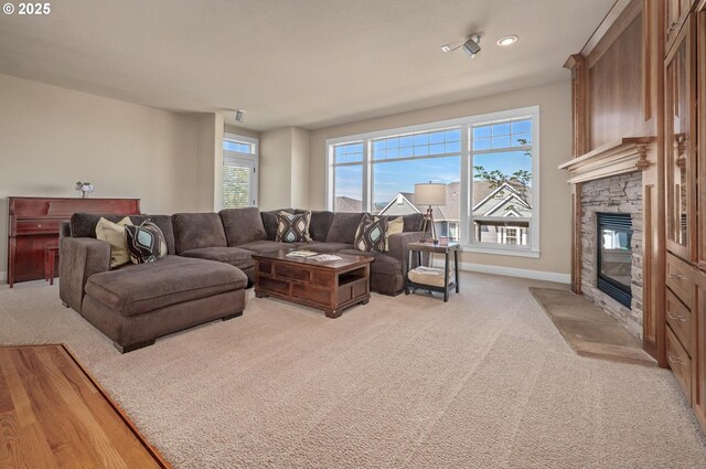 living area with a stone fireplace, light colored carpet, and baseboards