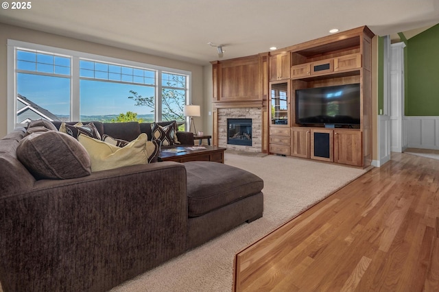 living room featuring light wood finished floors, a stone fireplace, wainscoting, and recessed lighting