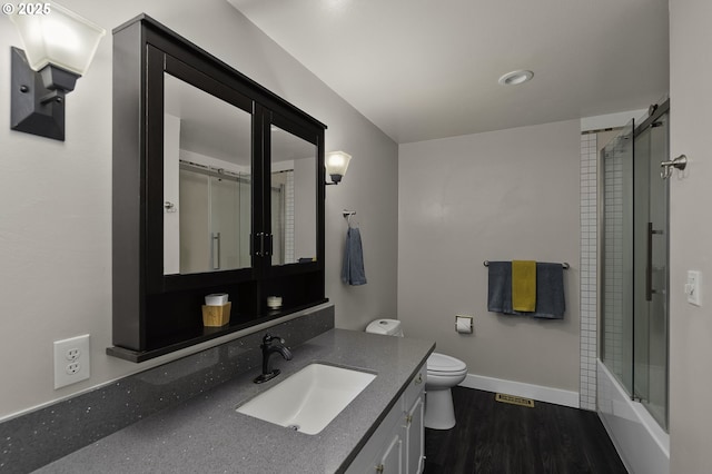 full bathroom featuring toilet, wood-type flooring, vanity, and bath / shower combo with glass door