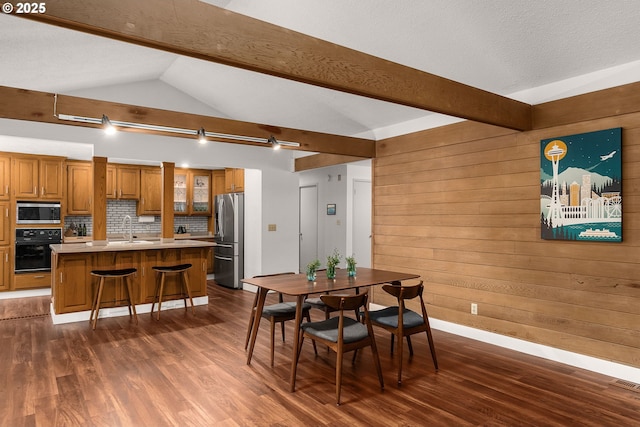 dining space with sink, dark hardwood / wood-style flooring, wooden walls, and vaulted ceiling