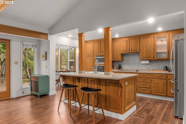 kitchen with stainless steel appliances, decorative columns, lofted ceiling, tasteful backsplash, and a center island with sink