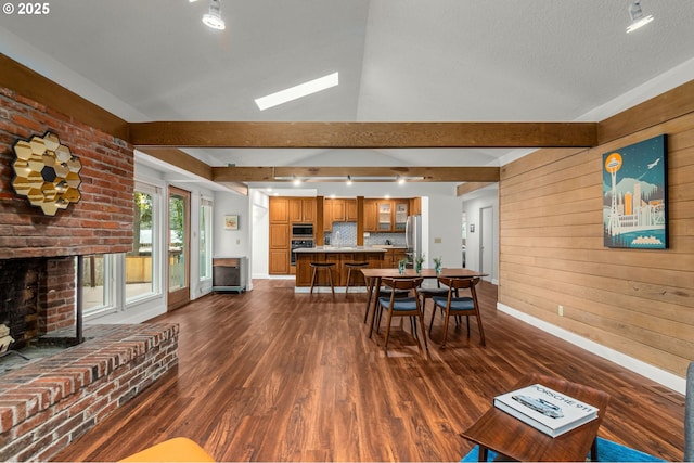 dining room featuring vaulted ceiling with beams, dark hardwood / wood-style floors, wood walls, and a fireplace