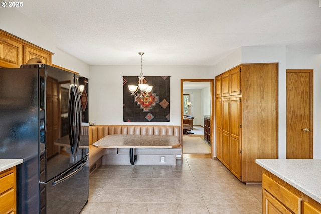 kitchen featuring pendant lighting, brown cabinets, light countertops, freestanding refrigerator, and an inviting chandelier