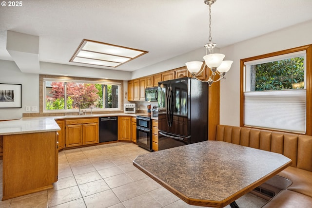 kitchen featuring brown cabinetry, pendant lighting, black appliances, a sink, and a notable chandelier