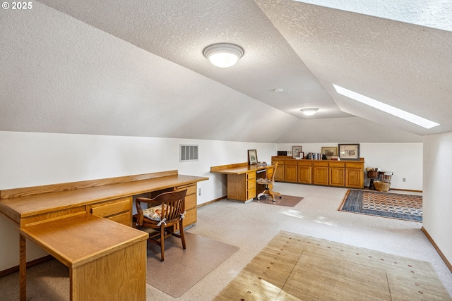 office area featuring vaulted ceiling with skylight, a textured ceiling, light colored carpet, visible vents, and baseboards