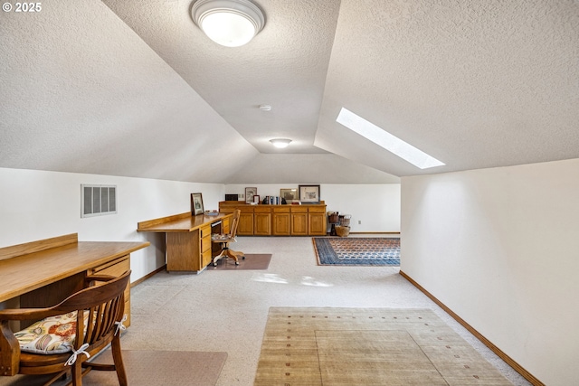 office space with visible vents, light carpet, baseboards, lofted ceiling with skylight, and a textured ceiling