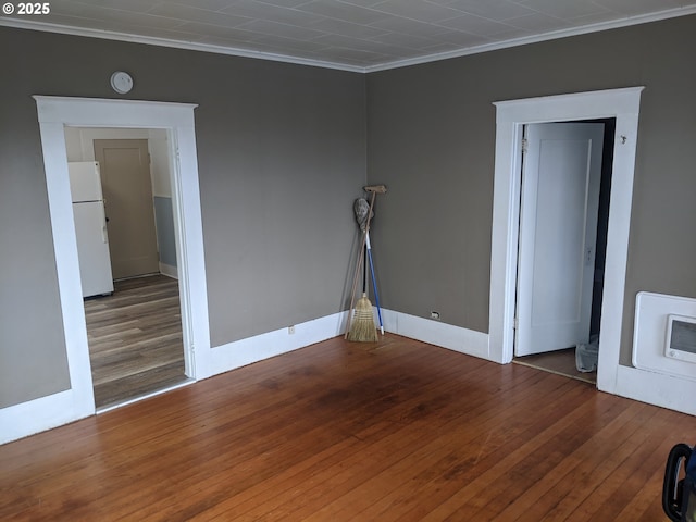 empty room with hardwood / wood-style floors, heating unit, and ornamental molding