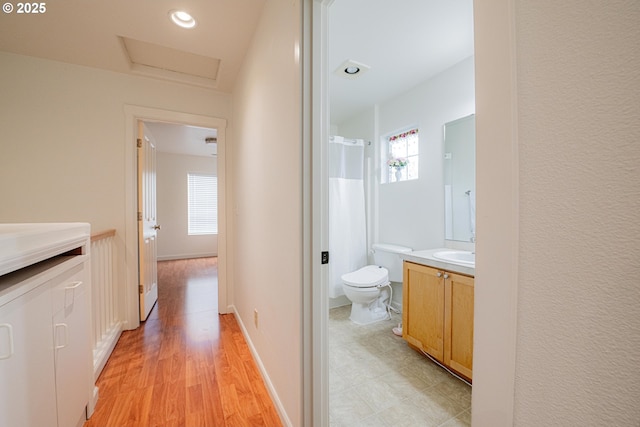 hall with light wood finished floors, plenty of natural light, attic access, and a sink
