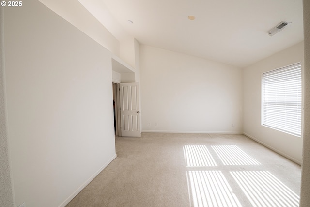 empty room with light carpet, vaulted ceiling, visible vents, and baseboards