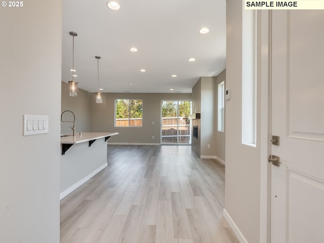 interior space with baseboards, recessed lighting, light countertops, a kitchen bar, and light wood-type flooring