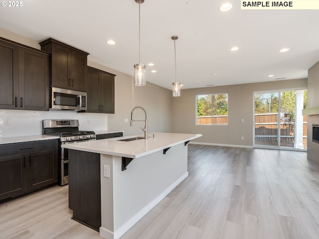 kitchen with backsplash, light countertops, light wood-type flooring, appliances with stainless steel finishes, and a sink