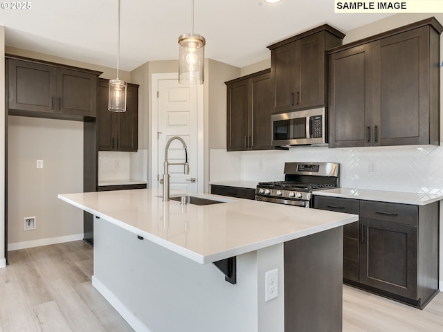 kitchen with a kitchen island with sink, sink, light wood-type flooring, decorative light fixtures, and stainless steel appliances