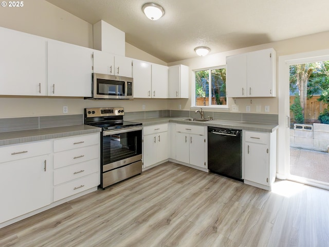 4549 SE Knapp St, Portland, OR 97206 - kitchen featuring appliances with stainless steel finishes, vaulted ceiling, light wood finished floors, white cabinets, and plenty of natural light