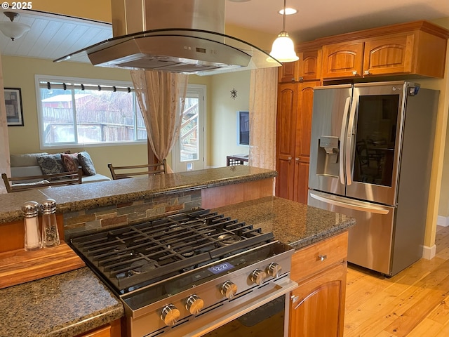 kitchen with dark stone countertops, brown cabinetry, appliances with stainless steel finishes, light wood-type flooring, and island range hood