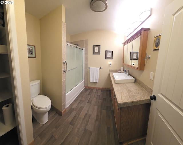 bathroom featuring toilet, wood finished floors, baseboards, enclosed tub / shower combo, and vanity