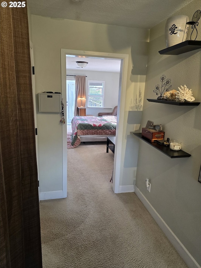 hallway featuring baseboards, light colored carpet, and a textured ceiling