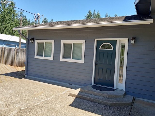 property entrance with crawl space, a shingled roof, and fence