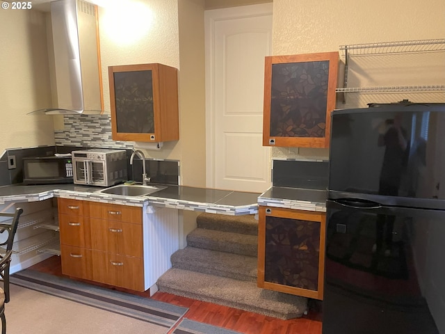 kitchen with backsplash, freestanding refrigerator, wood finished floors, brown cabinetry, and a sink