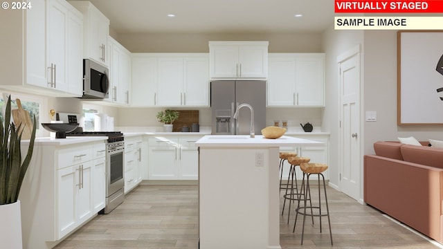 kitchen featuring light wood-type flooring, appliances with stainless steel finishes, white cabinetry, and a kitchen island with sink