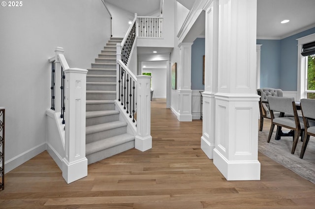 staircase featuring wood finished floors, ornate columns, crown molding, recessed lighting, and baseboards