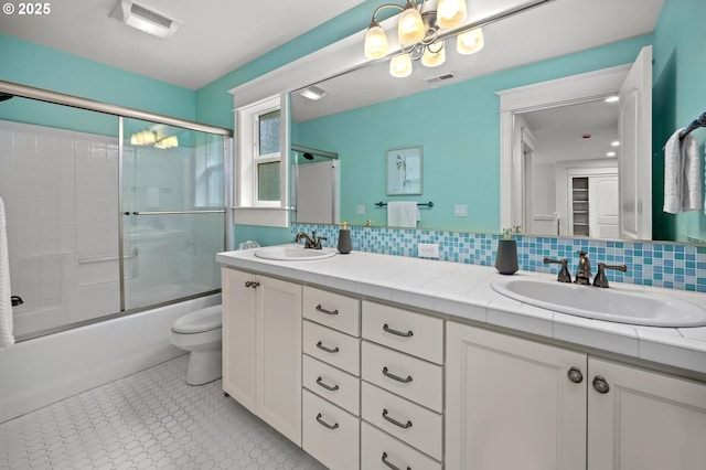 full bath with double vanity, shower / bath combination with glass door, backsplash, a chandelier, and toilet