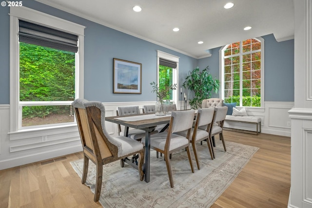dining space featuring ornamental molding, a wainscoted wall, recessed lighting, light wood-type flooring, and a decorative wall