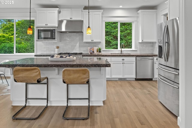 kitchen with appliances with stainless steel finishes, a sink, a breakfast bar area, white cabinets, and tasteful backsplash