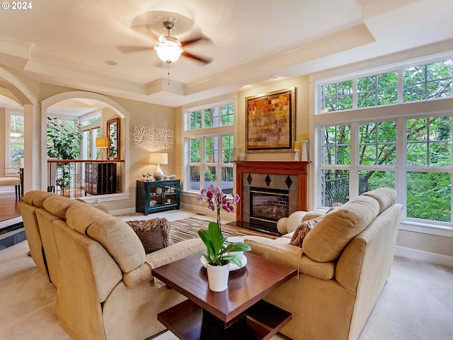 living room with a tray ceiling, a tile fireplace, ceiling fan, and crown molding