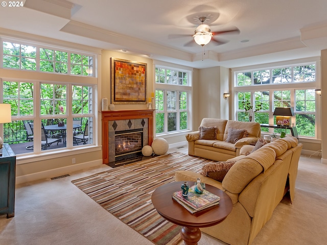 carpeted living room with a tile fireplace, a tray ceiling, ceiling fan, and ornamental molding