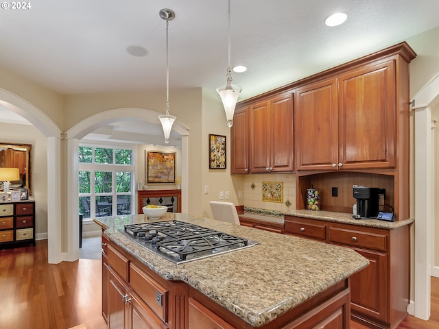 kitchen featuring stainless steel gas cooktop, wood-type flooring, decorative light fixtures, decorative backsplash, and a kitchen island