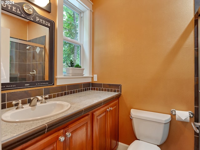 bathroom with backsplash, a shower with door, vanity, and toilet