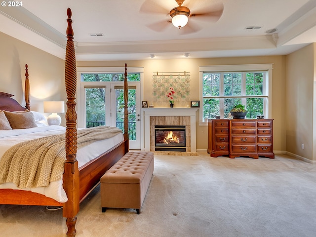 carpeted bedroom featuring access to exterior, ceiling fan, a raised ceiling, crown molding, and a fireplace