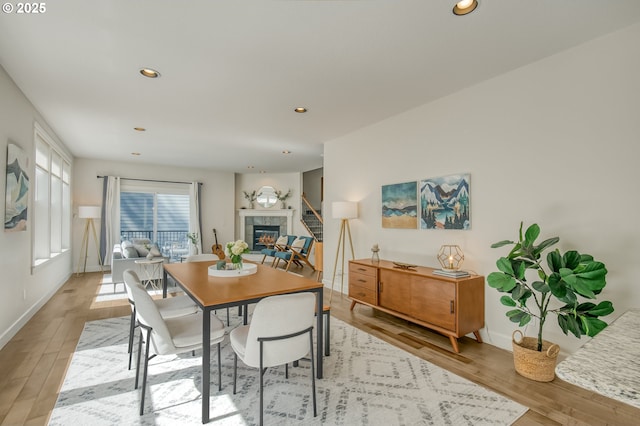dining area featuring a tiled fireplace, recessed lighting, baseboards, and light wood-type flooring