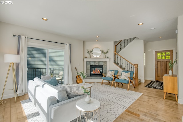 living room with recessed lighting, a tiled fireplace, light wood finished floors, and stairway