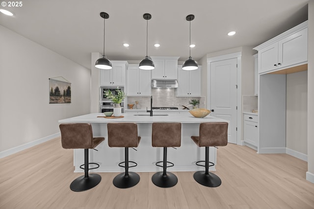 kitchen featuring a sink, light countertops, light wood-style floors, under cabinet range hood, and stainless steel oven