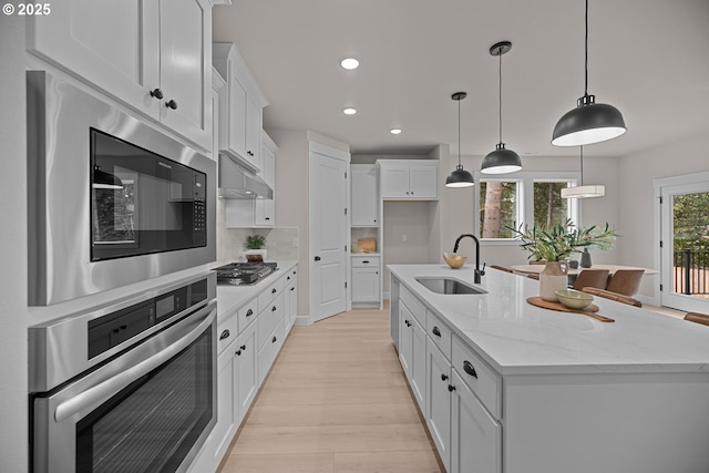 kitchen with built in microwave, under cabinet range hood, a center island with sink, stainless steel gas stovetop, and a sink