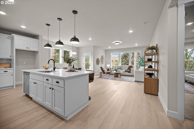 kitchen with a sink, light countertops, white cabinets, stainless steel dishwasher, and open floor plan