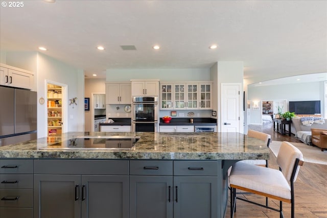 33685 Van Duyn Rd, Eugene, OR 97408 - kitchen with appliances with stainless steel finishes, light wood-type flooring, a spacious island, gray cabinets, and dark stone counters