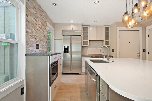 7752 SW Barnes Rd Unit B, Portland, OR 97225 - kitchen featuring built in appliances, a sink, light wood-type flooring, glass insert cabinets, and pendant lighting