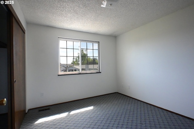 carpeted spare room featuring a textured ceiling and baseboards