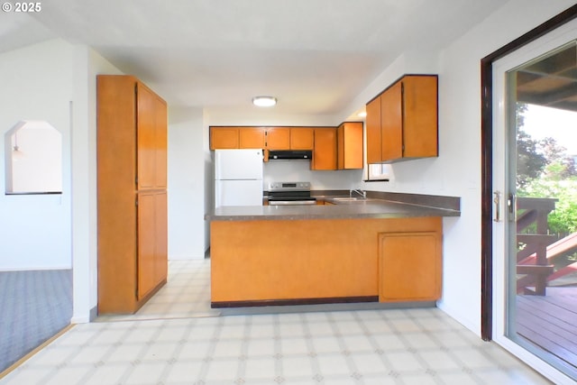 kitchen with freestanding refrigerator, under cabinet range hood, stainless steel electric stove, brown cabinetry, and dark countertops