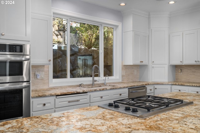 kitchen with a sink, decorative backsplash, stainless steel appliances, and white cabinetry