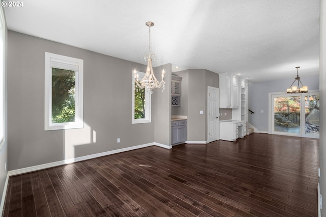 unfurnished dining area featuring baseboards, dark wood finished floors, and a chandelier