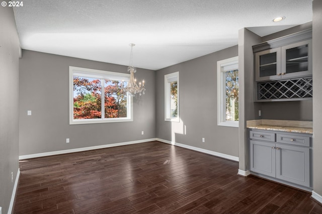 unfurnished dining area with baseboards, dark wood-type flooring, a notable chandelier, and a wealth of natural light