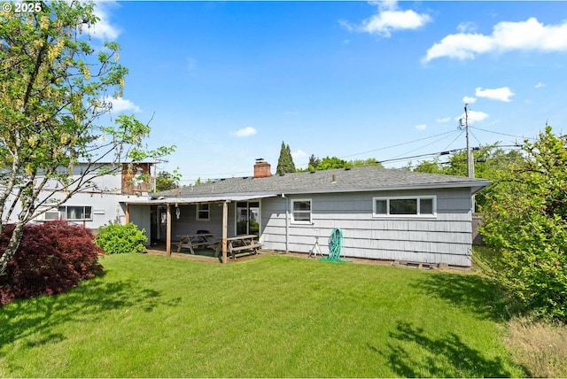 rear view of house featuring a yard, a chimney, a patio, and a shingled roof