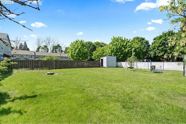 view of yard featuring a fenced backyard, a storage shed, a playground, and an outbuilding